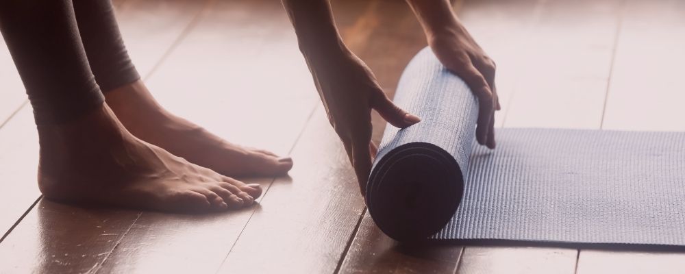 Woman unrolling a blue yoga mat onto a hardwood floor